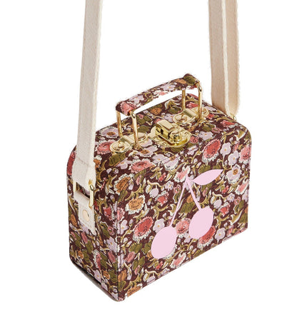 Girls’ Aimane Travel Bag by Bonpoint—a rectangular bag crafted from Liberty fabric with a floral pattern, featuring a cream strap, gold hardware, and a pink cherry graphic on the side.