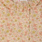A close-up of the Girls’ Melusina Blouse in Liberty Fabric by Bonpoint, highlighting its ruffled collar and button detail, adorned with a pink, green, and beige floral pattern on a light background.