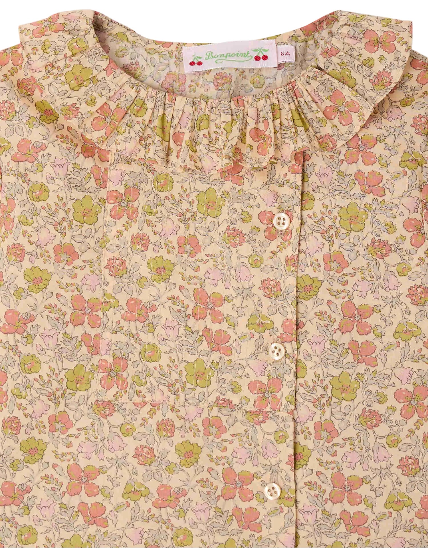 A close-up of the Girls’ Melusina Blouse in Liberty Fabric by Bonpoint, highlighting its ruffled collar and button detail, adorned with a pink, green, and beige floral pattern on a light background.
