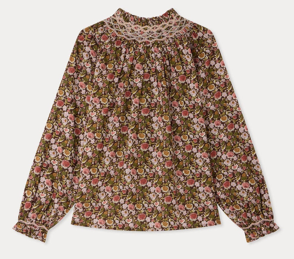 The Girls’ Petale Blouse by Bonpoint is a long-sleeve top featuring a floral pattern in pink, green, and brown hues, crafted from soft organic cotton. It is detailed with hand-embroidered smocking on the high neckline and gathered cuffs for an elegant touch.