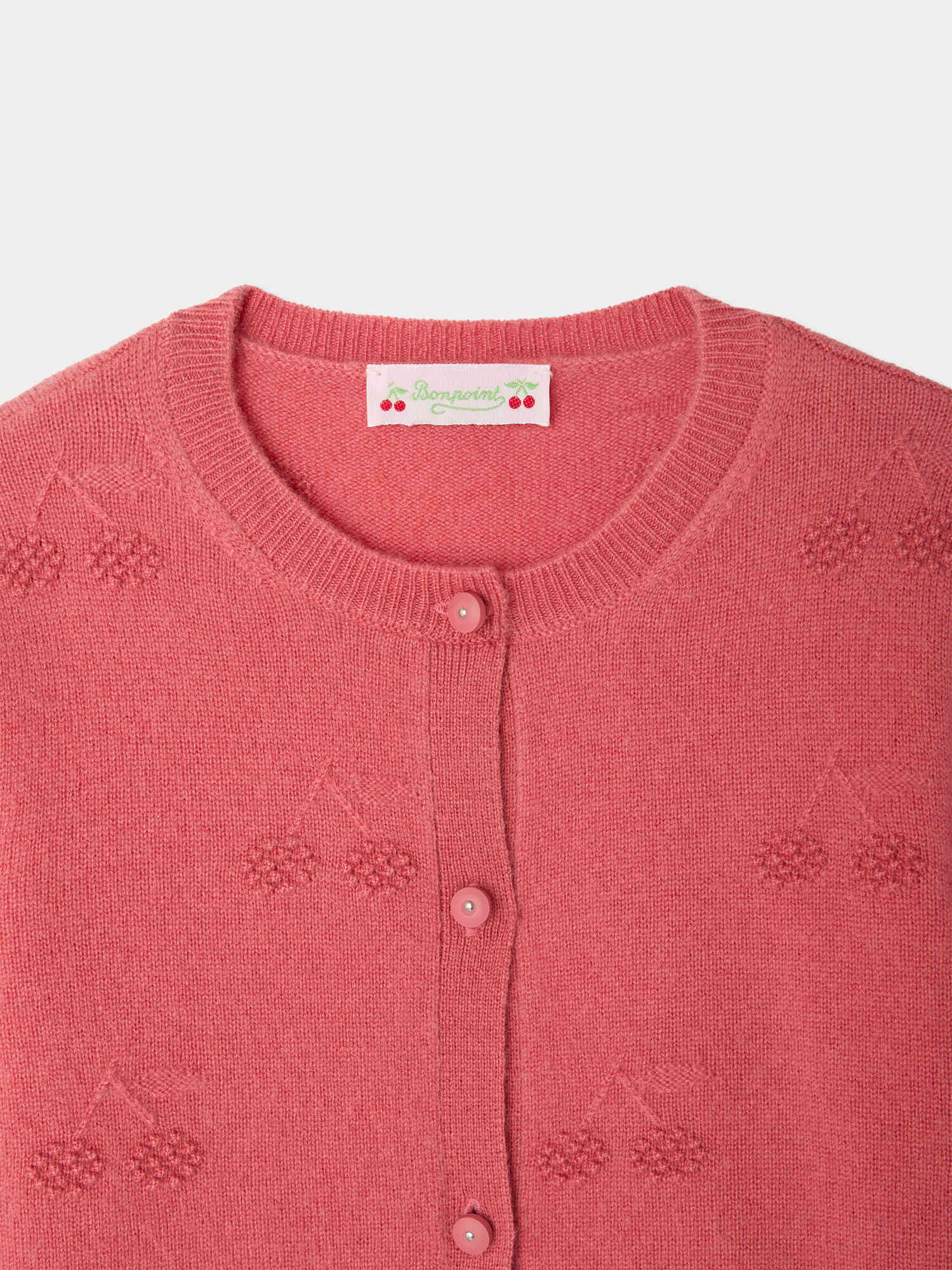 Close-up of the Bonpoint Girls’ Manon Cardigan, featuring a round neckline, cherry embroidery, and matching pink buttons. The signature Bonpoint label with cherries and text is sewn inside the collar, showcasing this cashmere cardigan’s distinctive style.