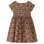 The Girls’ Duchesse Dress by Bonpoint features short sleeves and a floral print in pink, green, and brown hues. Made from soft organic cotton Liberty fabric, it is designed with a smocked bodice, three front buttons, and a gathered skirt.