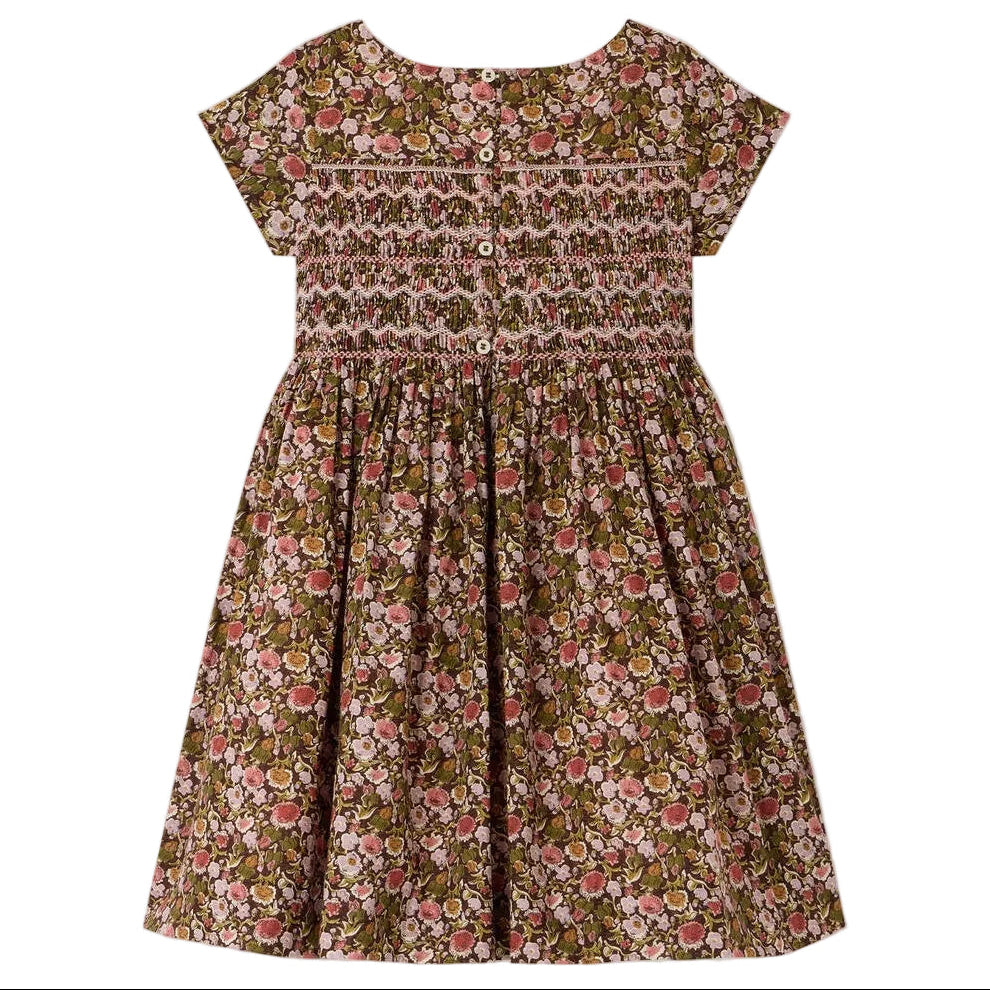 The Girls’ Duchesse Dress by Bonpoint features short sleeves and a floral print in pink, green, and brown hues. Made from soft organic cotton Liberty fabric, it is designed with a smocked bodice, three front buttons, and a gathered skirt.