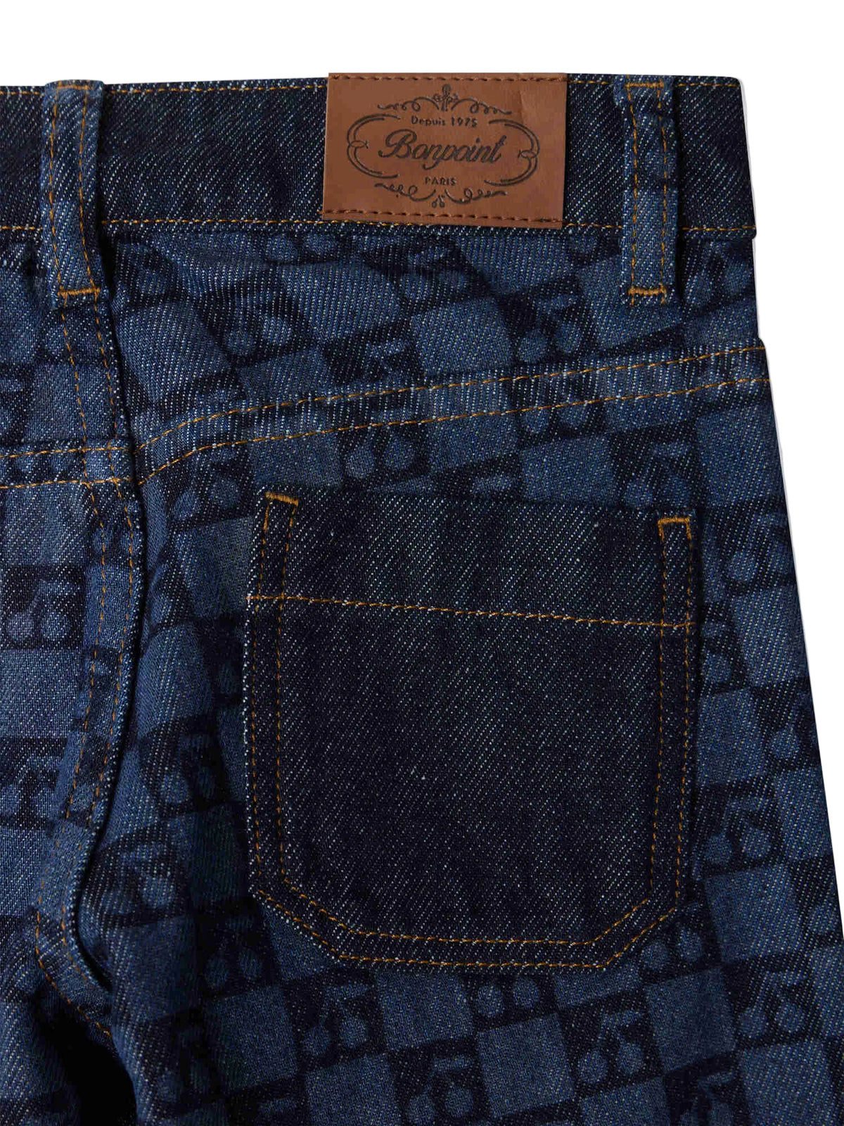 Close-up of the back pocket and waistband of the Bonpoint Girls’ Minalie Cherry Checkerboard-Print Denim Trousers, showcasing a brown leather brand label, adjustable high waist, and dark checkerboard pattern.