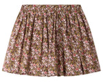 The Girls’ Suzon Skirt by Bonpoint is a knee-length, flared skirt for girls featuring a gathered waist and an all-over floral print in pink, red, and green hues set against a brown background.