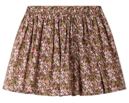 The Girls’ Suzon Skirt by Bonpoint is a knee-length, flared skirt for girls featuring a gathered waist and an all-over floral print in pink, red, and green hues set against a brown background.