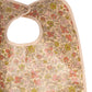 A close-up of the Bonpoint Clip-on Bib in Yellow Liberty Fabric, showcasing a charming floral pattern in shades of pink, red, and green on soft Liberty fabric with a convenient neck opening.