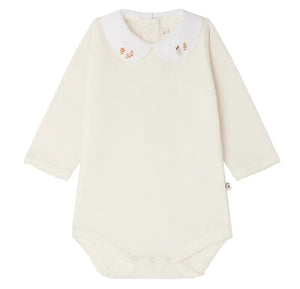 Bonpoint’s Baby Cygne LS Bodysuit is a long-sleeved, cream-colored piece crafted from soft organic cotton. It features a white Peter Pan collar delicately hand-embroidered with small florals and has convenient snap closures at the bottom.