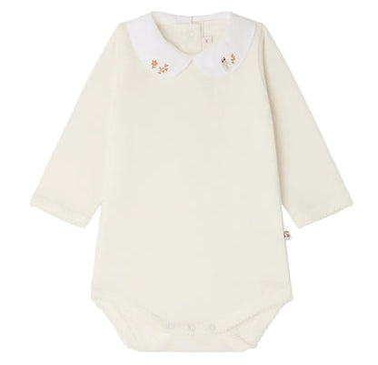 Bonpoint’s Baby Cygne LS Bodysuit is a long-sleeved, cream-colored piece crafted from soft organic cotton. It features a white Peter Pan collar delicately hand-embroidered with small florals and has convenient snap closures at the bottom.