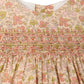 Close-up of the Bonpoint Baby Girls’ and Girls’ Maruska Dress, crafted from Liberty fabric and adorned with pink, green, and yellow floral patterns, featuring intricate hand-embroidered pink and orange smocking across the chest.