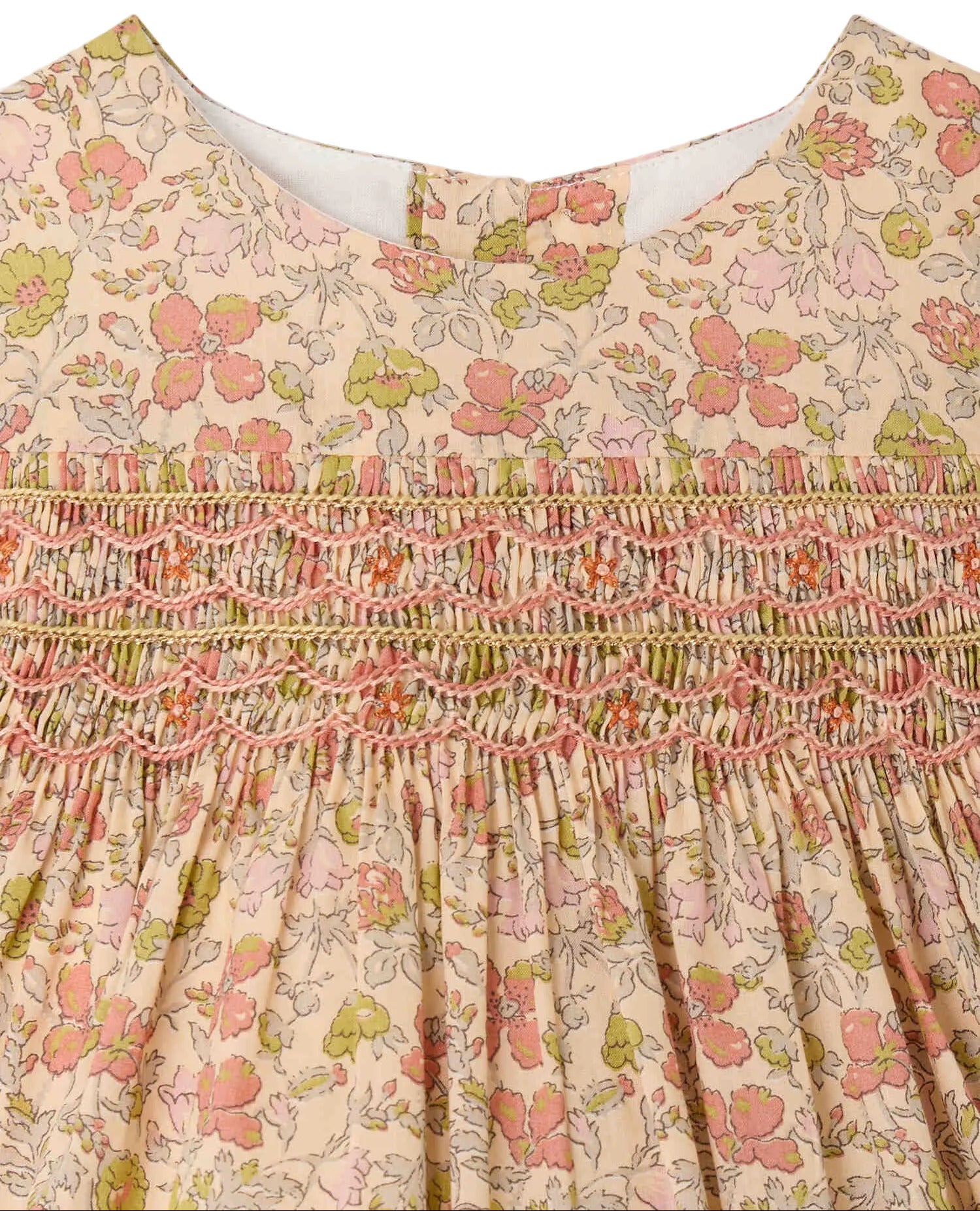 Close-up of the Bonpoint Baby Girls’ and Girls’ Maruska Dress, crafted from Liberty fabric and adorned with pink, green, and yellow floral patterns, featuring intricate hand-embroidered pink and orange smocking across the chest.
