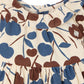 Close-up of the Bonpoint Baby Girls’ Melyssa Dress with Cherry Print, featuring a cream-colored background adorned with brown and blue cherries, a gathered waist, round collar, and two white shoulder buttons. Crafted from soft organic cotton corduroy for a cozy feel.