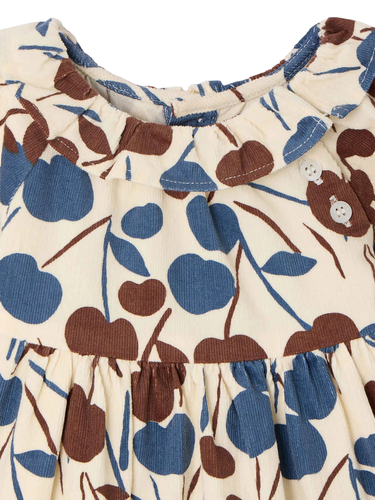 Close-up of the Bonpoint Baby Girls’ Melyssa Dress with Cherry Print, featuring a cream-colored background adorned with brown and blue cherries, a gathered waist, round collar, and two white shoulder buttons. Crafted from soft organic cotton corduroy for a cozy feel.