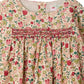 A close-up of the Bonpoint Baby Girls’ and Girls’ Félicie Dress with Smocking and Hand Embroidery, showcasing its delicate floral motif in pink, red, and green hues, hand-embroidered smocked detailing across the chest, and a classic round neckline.
