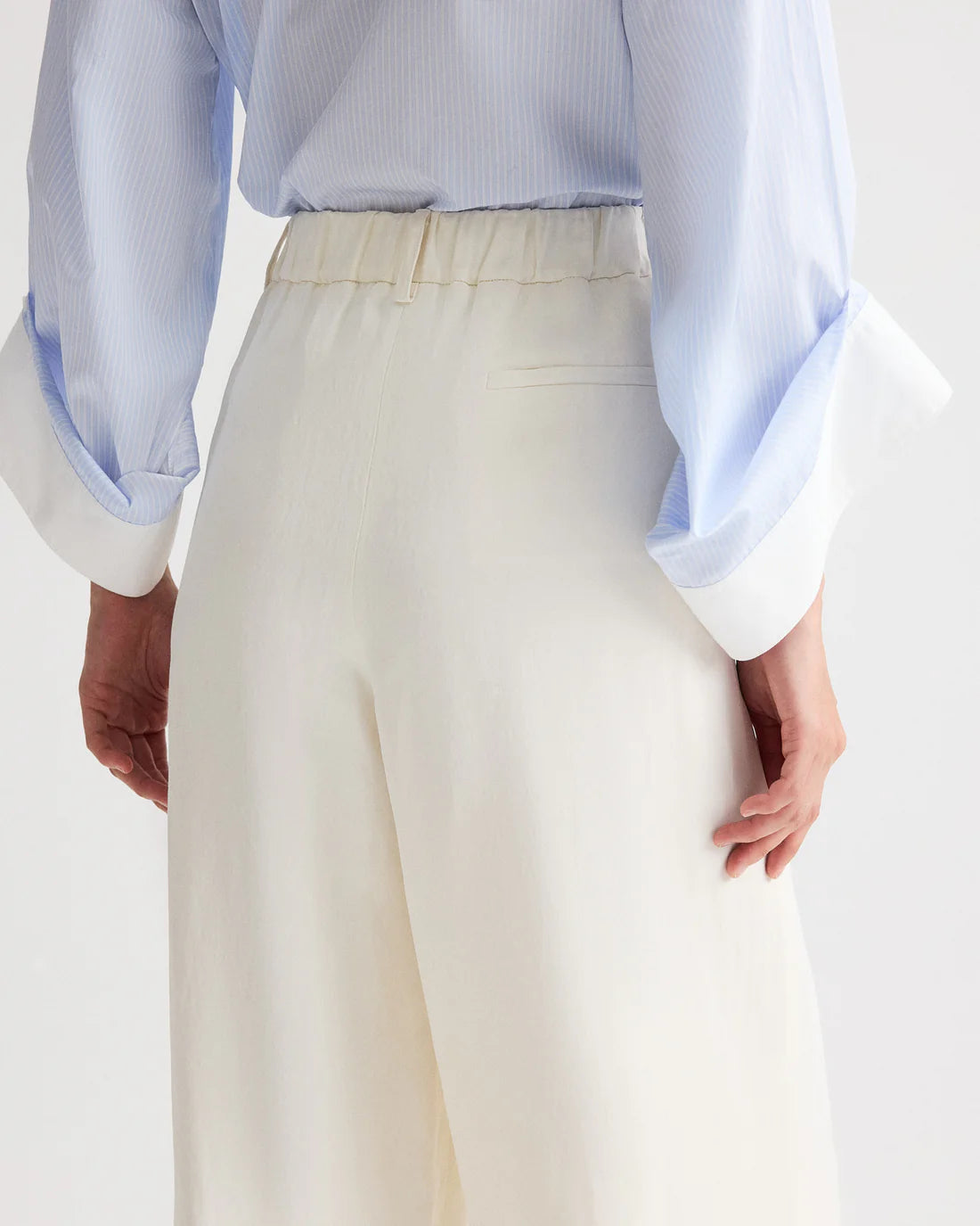 Person shown from the back wearing TWP's Hudson St Pant in white, paired with a light blue, long-sleeved shirt, hands resting by their sides.