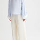 A person stands facing away, wearing TWP’s Hudson St Pant—relaxed mid-rise, wide-leg pants in a coated viscose linen blend—paired with a light blue long-sleeve shirt with white cuffs, set against a plain light background.