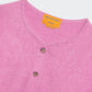 A close-up of the Grizzly Cashmere Cardigan by Guest in Residence, a pink women's knitwear piece featuring brown buttons and an orange "Guest in Residence" label at the neckline.