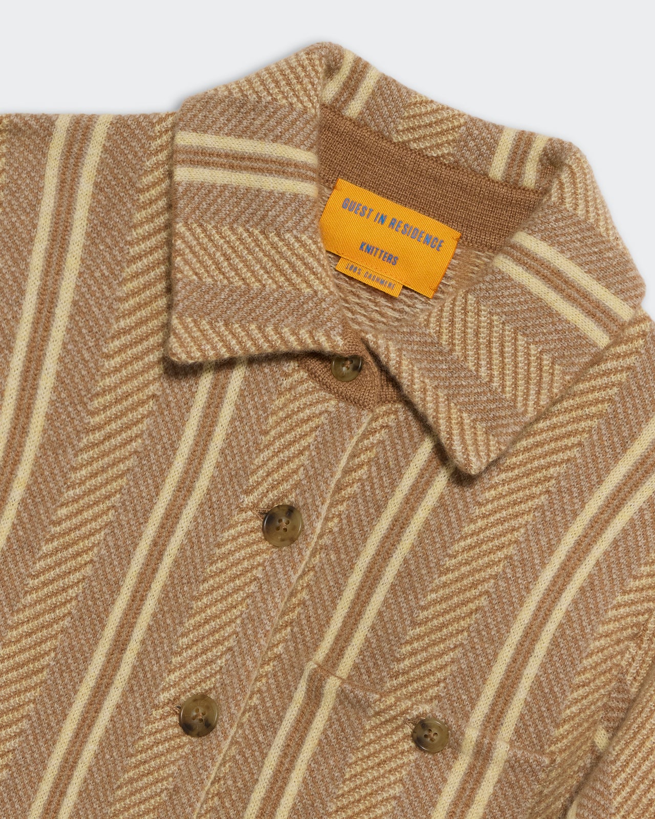 Close-up of the Dylan Stripe Shirt by Guest in Residence, a brown and beige striped button-down with herringbone pattern and yellow brand label on the collar. Layer over a soft cashmere sweater for extra warmth and style.