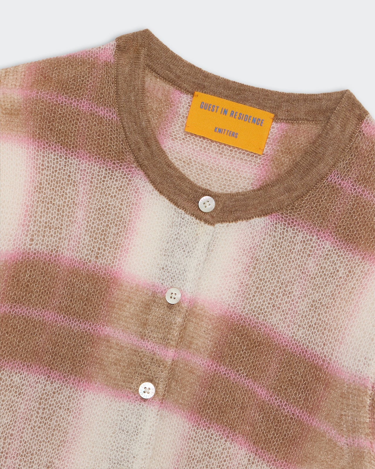 A close-up of the Guest in Residence Shadow Plaid Cardigan, a fuzzy cashmere blend in beige, white, and pink stripes with white buttons and a visible inside collar label.