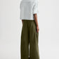Person standing against a white background, wearing the TWP Tie One On Shirt—a light-colored cropped button down with rolled sleeves—and wide-leg olive green pants made from vintage washed poplin.