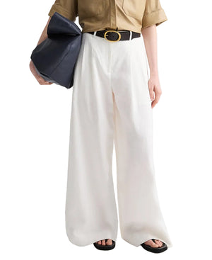 Person wearing a tan shirt tucked into TWP Avery Pants—high-waisted white relaxed fit trousers—styled with a black belt, large black bag, and black sandals.