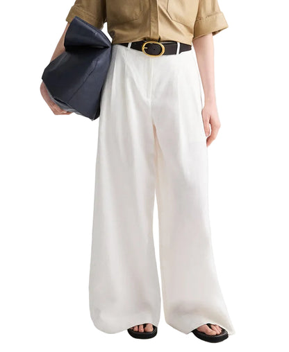 Person wearing a tan shirt tucked into TWP Avery Pants—high-waisted white relaxed fit trousers—styled with a black belt, large black bag, and black sandals.
