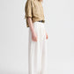 A person wears the TWP Avery Pant, styled with a loose tan button-up shirt, black belt, and black sandals, standing against a plain light background.