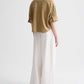 A person stands facing away against a plain light background, wearing TWP's Avery Pant with a loose tan short-sleeve shirt and relaxed fit.