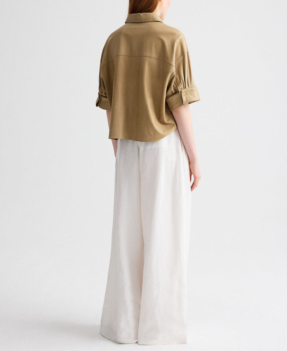 A person stands facing away against a plain light background, wearing TWP's Avery Pant with a loose tan short-sleeve shirt and relaxed fit.