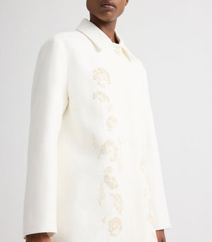 A model wears the TWP Edinburgh Coat, a knee-length car coat featuring a collar and subtle light floral embroidery on the front, photographed from the shoulders down against a plain background.