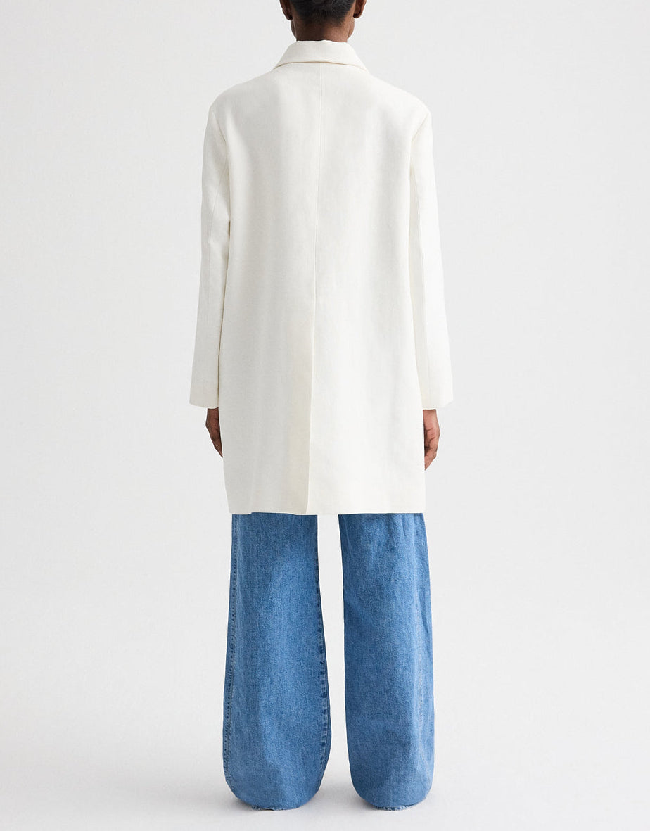 A person stands facing away against a plain light background, wearing the TWP Edinburgh Coat and wide-leg blue jeans.