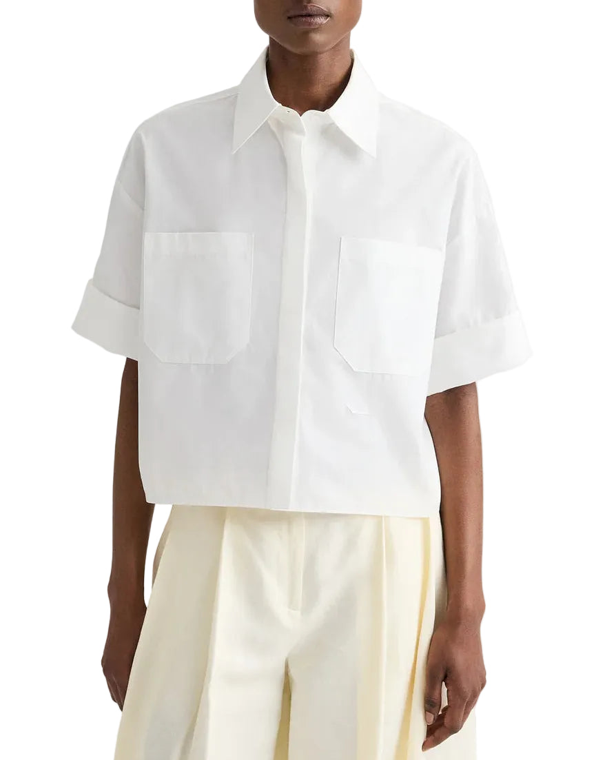 Someone dressed in the TWP My Newest Mistake Shirt, an Italian cotton, relaxed-fit short-sleeve button-up with two front pockets, paired with cream pleated trousers.