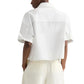 A person is shown from the back wearing the TWP My Newest Mistake Shirt, featuring a relaxed fit, Italian cotton, short sleeves, and paired with cream-colored pants against a plain background.
