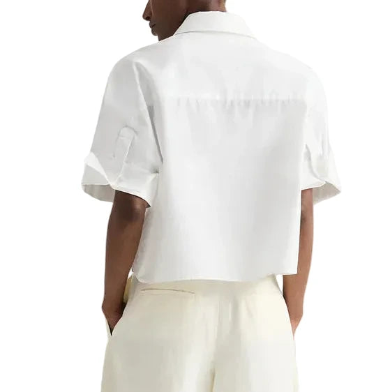 A person is shown from the back wearing the TWP My Newest Mistake Shirt, featuring a relaxed fit, Italian cotton, short sleeves, and paired with cream-colored pants against a plain background.