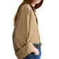 A person with long red hair models the TWP Beau Shirt in tan Supima cotton, styled with rolled sleeves and blue jeans, shown from the side against a white background.