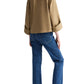 A person stands with their back to the camera, wearing a tan jacket over the TWP Beau Shirt, blue jeans, and brown shoes.