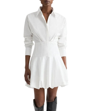 A person in the TWP Mila Dress—a long-sleeve, collared white cotton shirt dress with a fitted waist and flared skirt—paired with black knee-high boots.