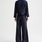 A person stands with their back to the camera, wearing the TWP Next Ex Ruffle Top—a loose-fitting, dark blue long-sleeve top—paired with matching wide-leg pants featuring a cropped boxy silhouette, set against a plain light background.