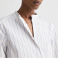 Model wears the Tied Down Stripe Shirt by TWP, featuring light blue and white vertical stripes, a band collar, and a partially unbuttoned front against a plain background.
