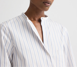 Model wears the Tied Down Stripe Shirt by TWP, featuring light blue and white vertical stripes, a band collar, and a partially unbuttoned front against a plain background.