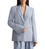 A woman wears the TWP Her Fit Blazer in light gray, an oversized single-breasted style with wide sleeves, paired with matching pants against a plain background.