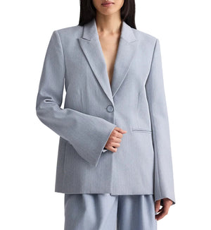 A woman wears the TWP Her Fit Blazer in light gray, an oversized single-breasted style with wide sleeves, paired with matching pants against a plain background.