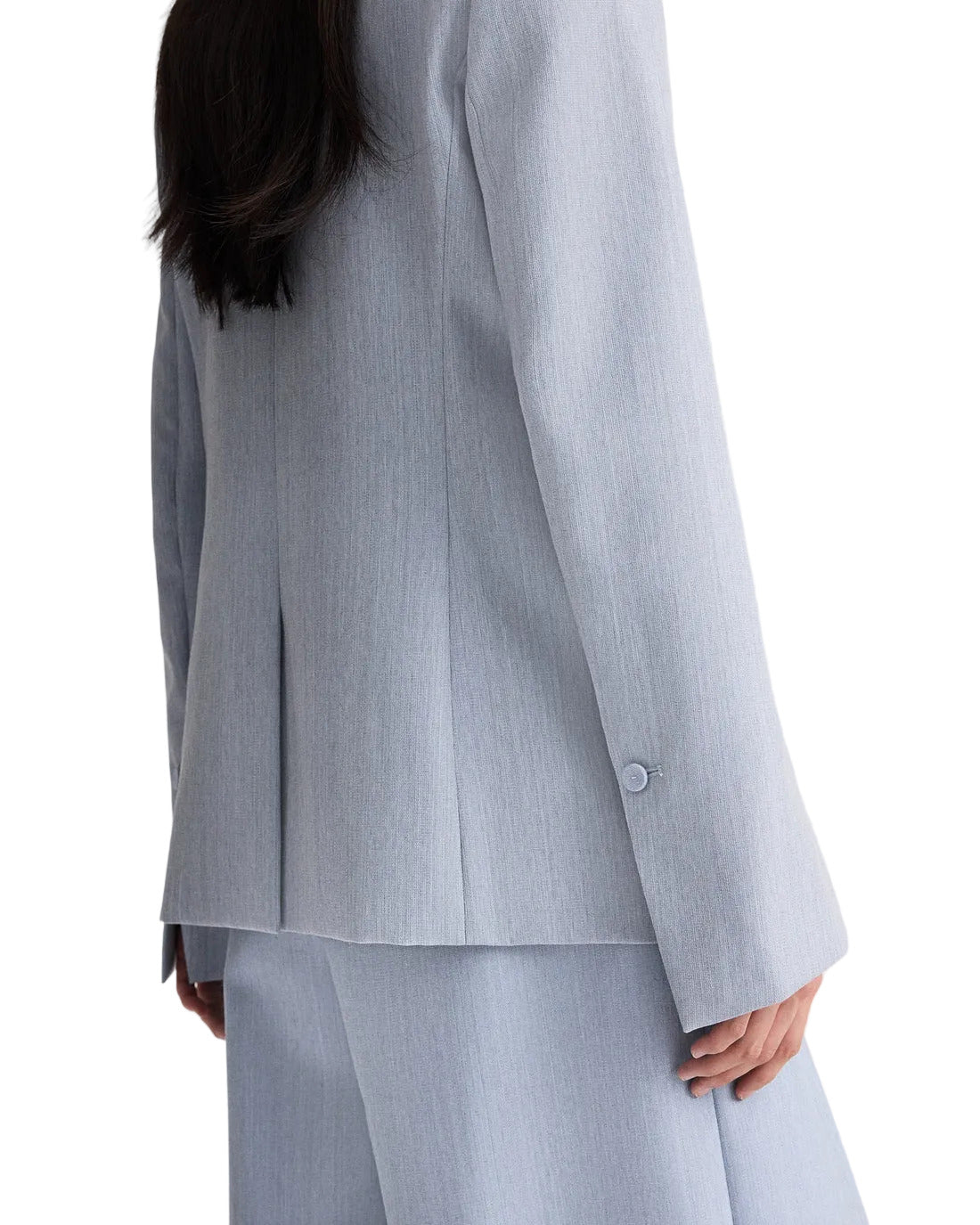 A person with long dark hair, seen from behind, wears the TWP Her Fit Blazer in light gray, arms relaxed at their sides.