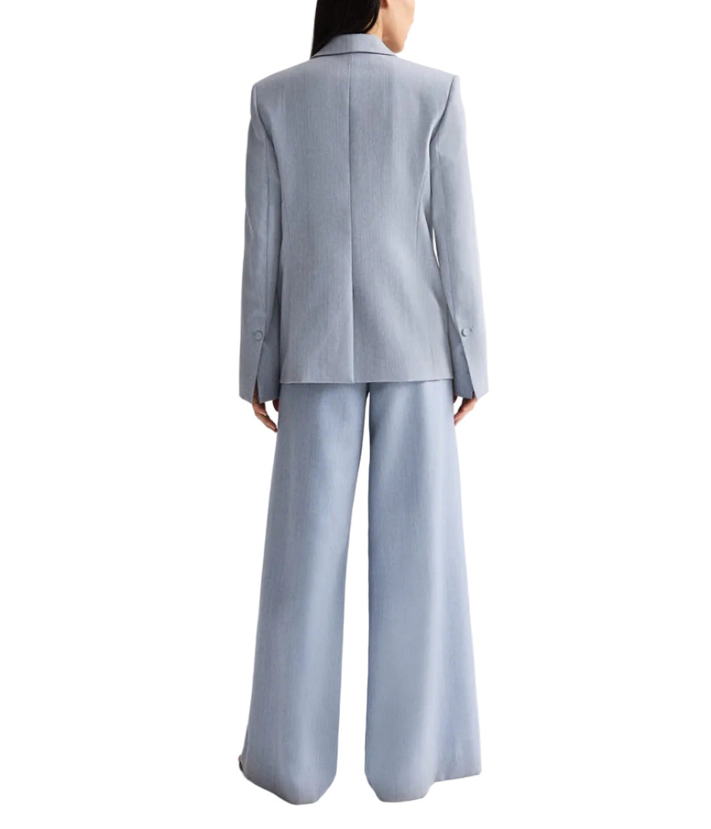 A woman faces away, wearing the TWP Her Fit Blazer in light blue with matching wide-leg trousers against a white background.