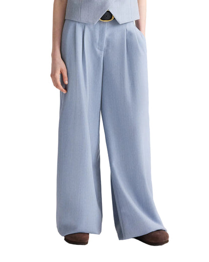 A person wearing the TWP Avery Pant, loose-fitting light blue wide-leg wool trousers, paired with brown shoes, shown from the shoulders down.