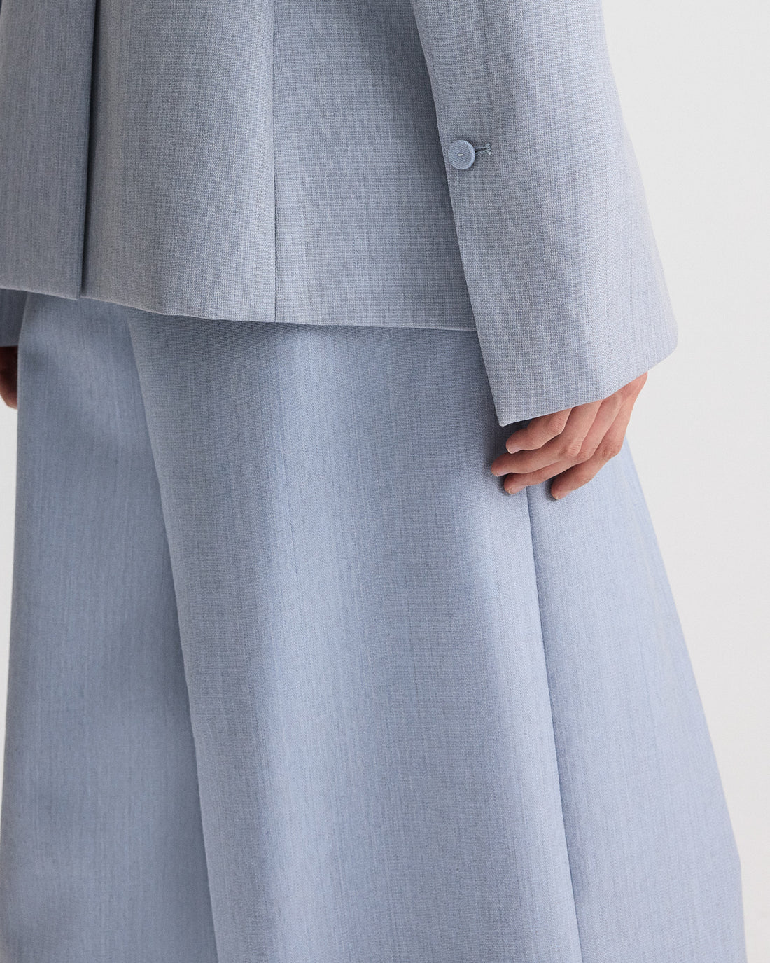 Model wearing TWP's Avery Pant in light blue wool suiting, featuring wide-leg trousers, shown from mid-torso to knees with hand at side.