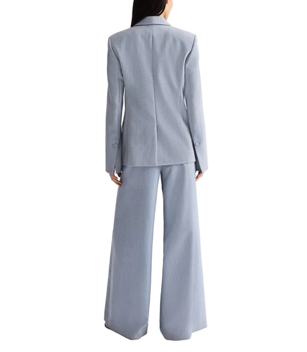 A person wearing the TWP Avery Pant—a light blue pleated wide-leg trouser—paired with a fitted blazer, viewed from the back against a white background.