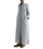 A person wearing the TWP Jenny's Glossy Mini Stripe Gown, an oversized light gray shirtdress with a collar and long sleeves, paired with olive green boots.