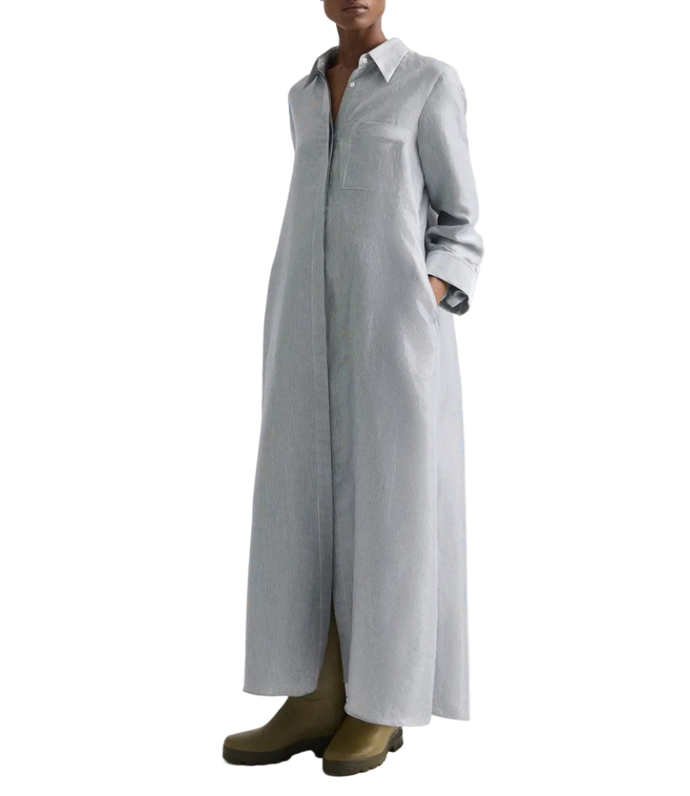 A person wearing the TWP Jenny's Glossy Mini Stripe Gown, an oversized light gray shirtdress with a collar and long sleeves, paired with olive green boots.