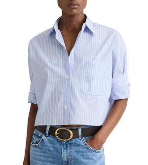 A person wears the TWP Next Ex Stripe Shirt with rolled sleeves, paired with medium-wash jeans and a black belt featuring a gold oval buckle.